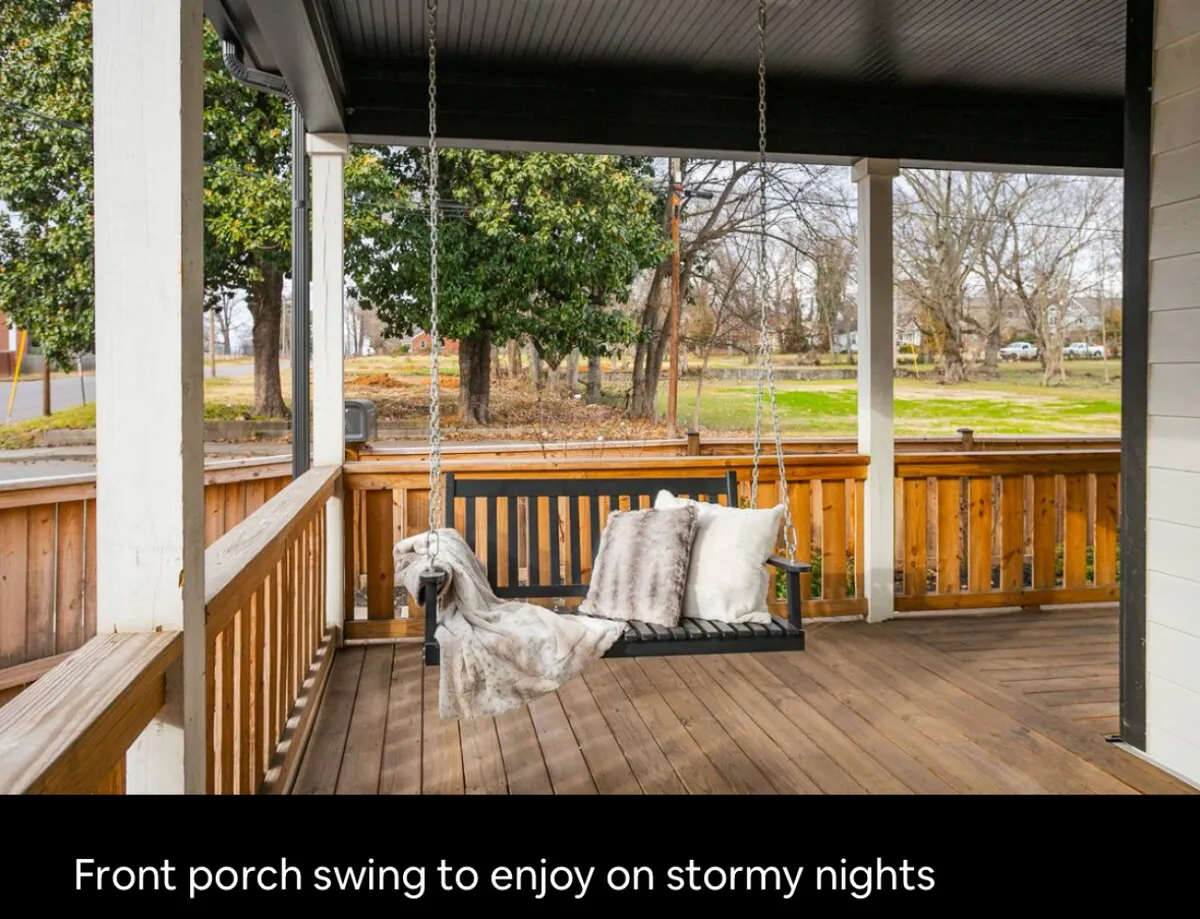 A cozy porch swing with decorative pillows sits on a wooden railing, offering a peaceful spot to relax, read, or enjoy the outdoors. This inviting space connects the home to its leafy neighborhood setting, encouraging moments of leisure and reflection.