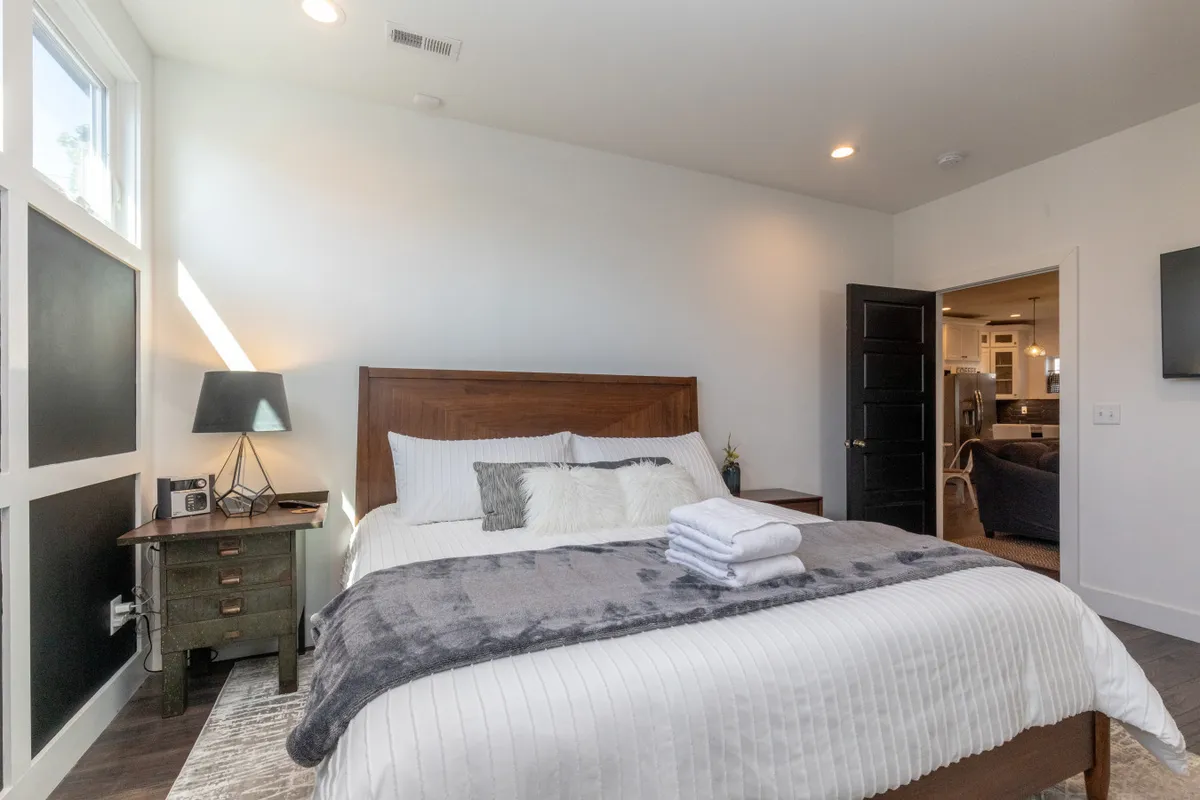 A serene bedroom with a plush bed, soft bedding, a nightstand with a lamp, and a textured throw blanket. Gentle natural light filters into the space, emphasizing a calm and restful atmosphere.