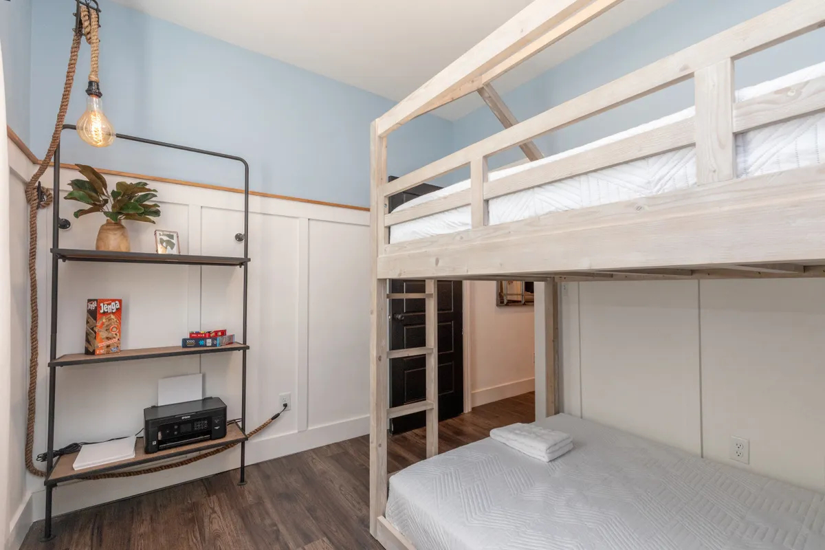 A cheerful and practical double bunk room featuring two sets of bunk beds, a shelving unit, and a decorative plant. The space is designed for both sleep and play, offering flexible, family-friendly accommodations.