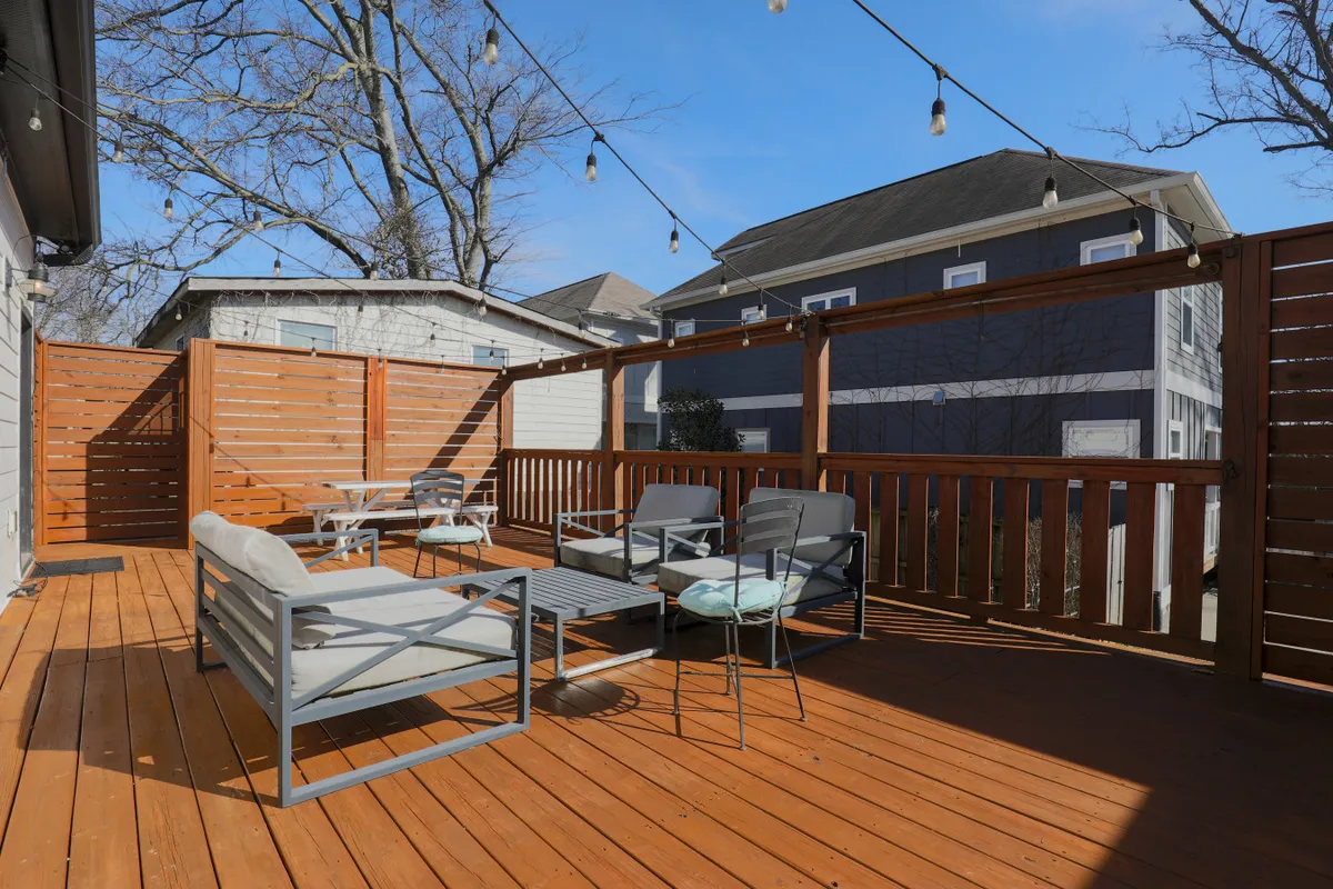 This image shows a wooden deck set up with comfortable outdoor seating and string lights overhead, creating a warm, inviting ambiance. The deck appears spacious and ready for gatherings, with an open view into the backyard area.