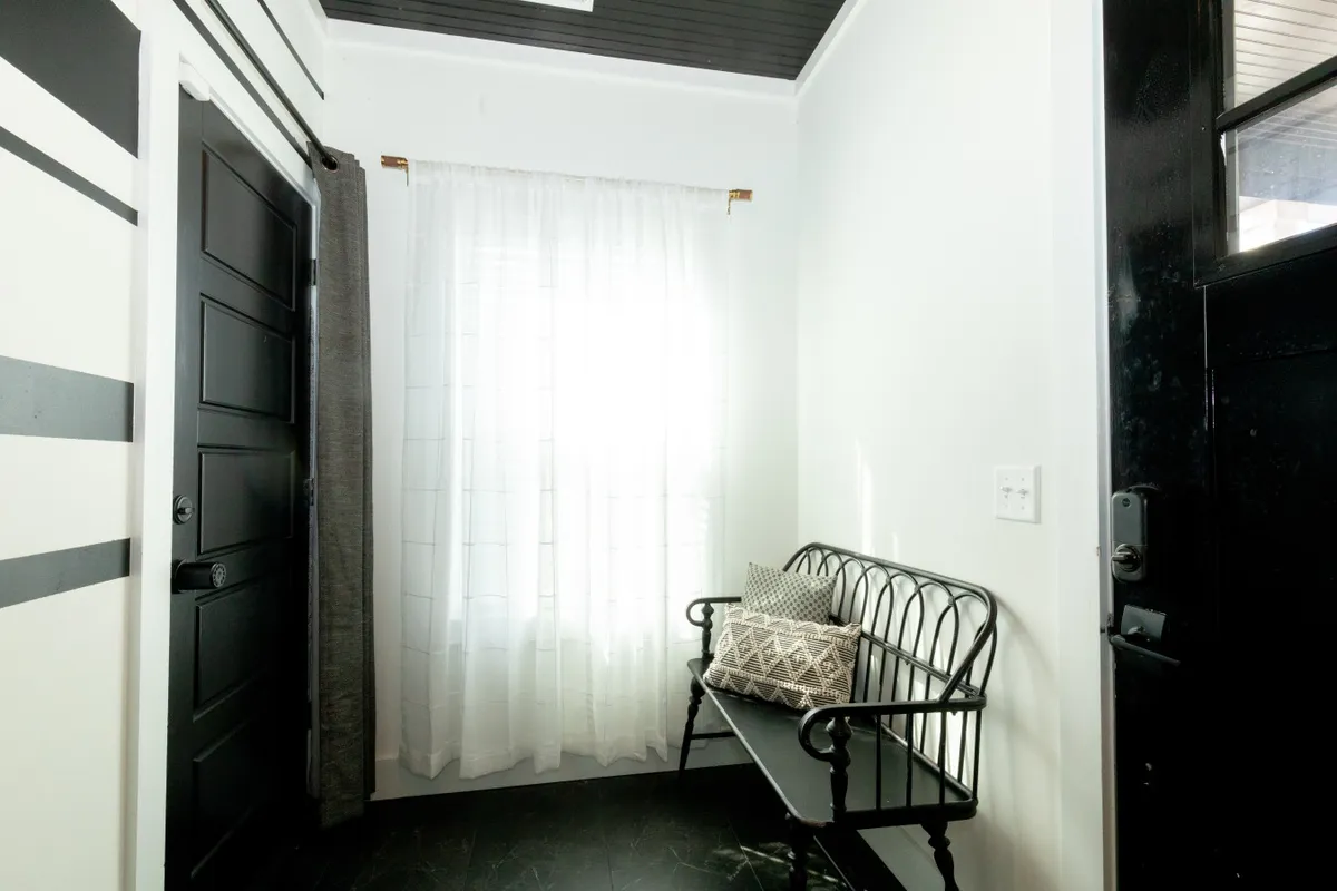This image features a stylish black door, a cushioned bench, and soft curtains. The setup provides a cozy waiting or greeting area that feels both practical and inviting.