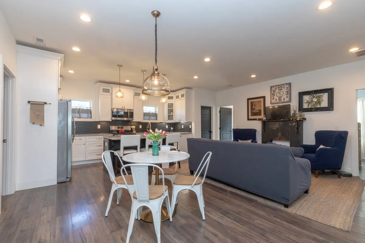 This image captures an open-concept space featuring the kitchen island, dining table, cozy couch, and a fireplace, all within a single cohesive shot. The layout highlights the integration of cooking, dining, and lounging areas, making it perfect for gatherings and relaxed evenings. Soft lighting and warm decor create an inviting, homey ambiance.