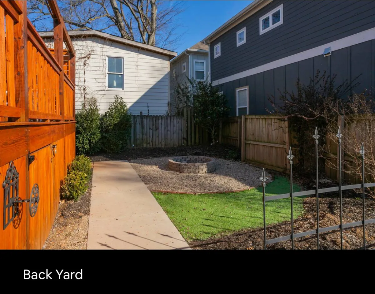 The scene features a wooden deck overlooking a grassy backyard with a fire pit and a clear pathway. The area is set up for gatherings, with space for relaxing, playing, and hosting barbecues or evening get-togethers.